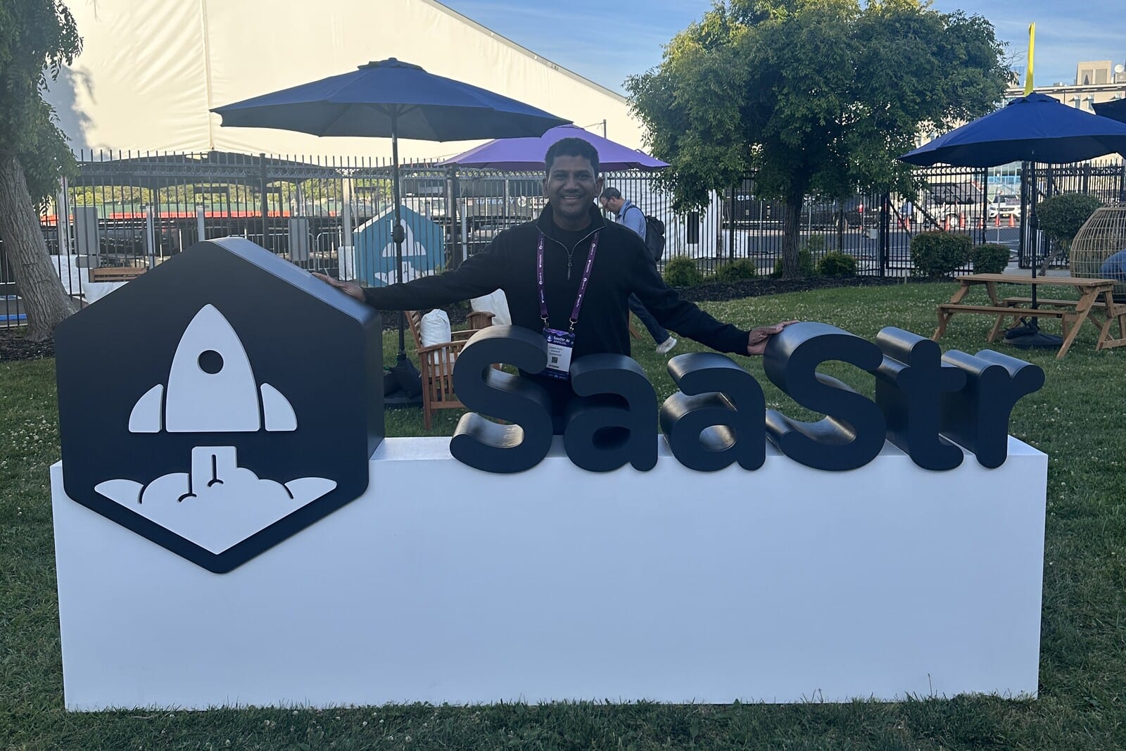 Deepak Gupta standing beside the SaaStr rocket logo and letter sign on the lawn outside the venue